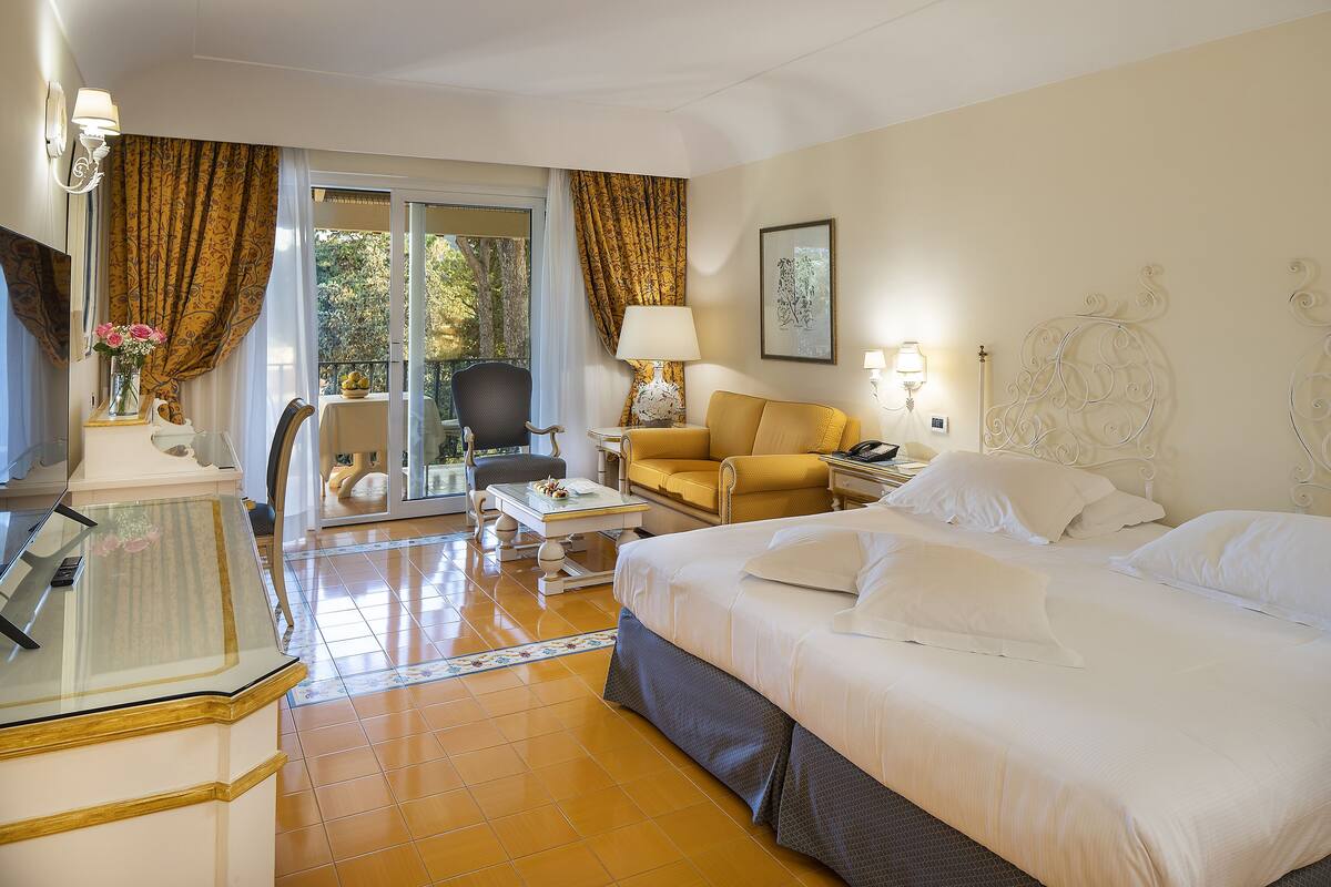 Ein Hotelzimmer mit Bett, Sofa, Schreibtisch mit Lampe, Stuhl und Blick ins Freie.