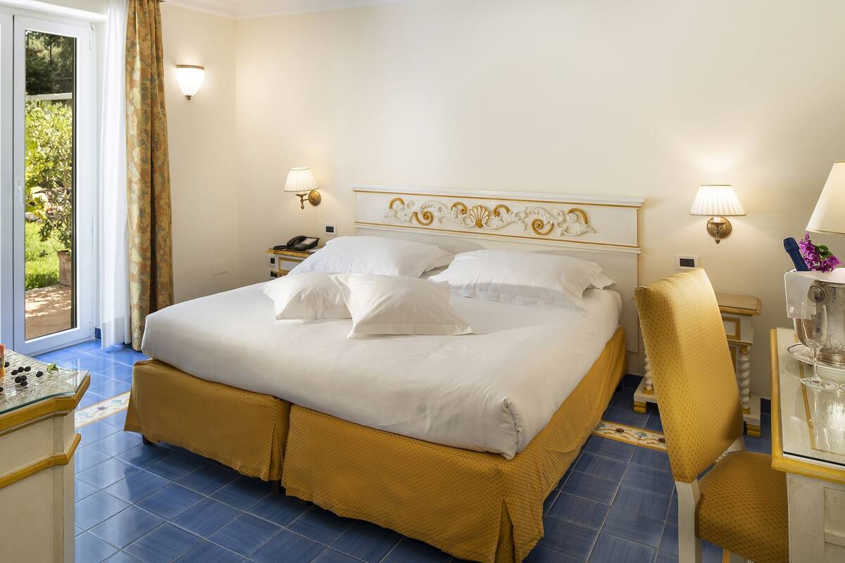 Ein Hotelzimmer mit einem großen Bett, zwei Nachttischen, einem Sessel und einem kleinen Tisch mit einer Lampe.