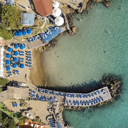 An aerial view of a beachside resort with multiple sun loungers, umbrellas, and a wooden deck overlooking the sea.