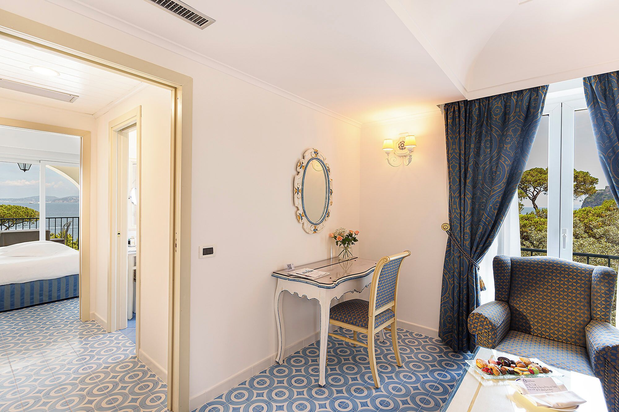 Habitación de hotel con cama, escritorio, silla y mesa de comedor con vista al mar.