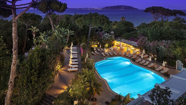 A swimming pool with lounge chairs and umbrellas, surrounded by trees and overlooking a body of water. - Excelsior Belvedere Hotel & Spa (Ischia)
