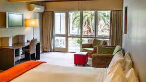 Een hotelkamer met een bed, een bureau met een lamp, een televisie en een groot raam met gordijnen.