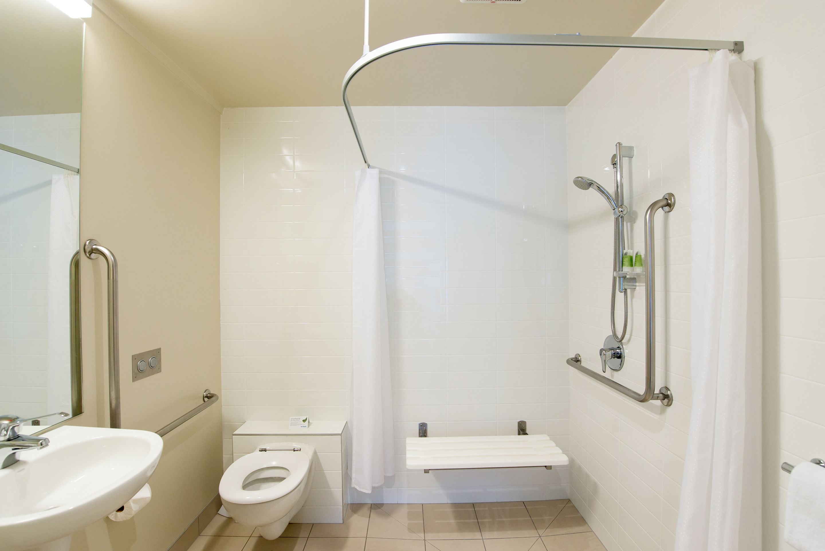 A modern bathroom with a toilet, sink, shower, and grab bars.