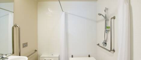 A modern bathroom with a toilet, sink, shower, and grab bars.