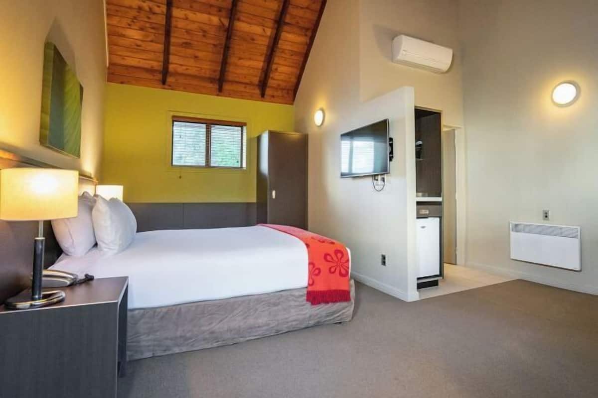 A bedroom with a bed, bedside table, lamp, and a television on the wall.