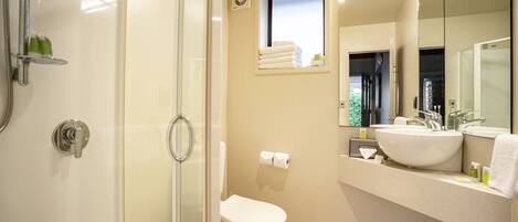 A modern bathroom with a glass shower enclosure, a toilet, a sink with a mirror, and a window providing natural light.