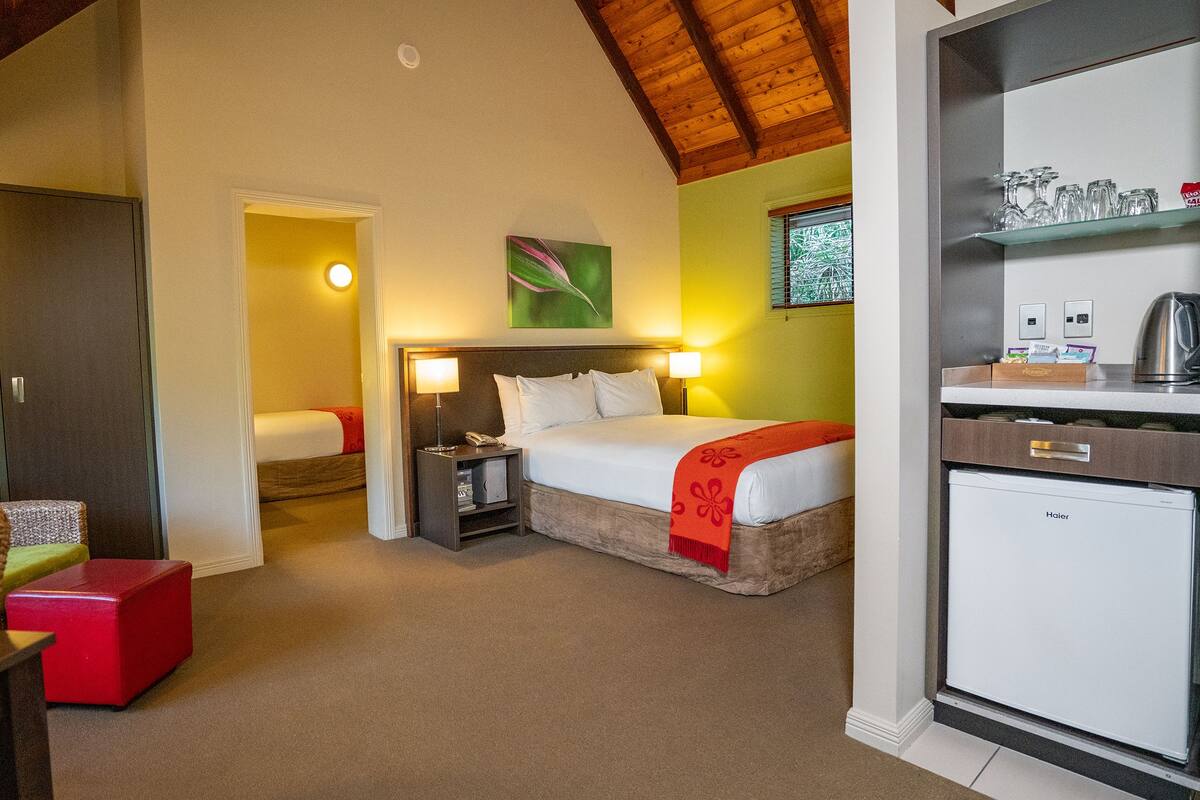 A hotel room with a bed, bedside tables, a desk, a chair, and a kitchenette.