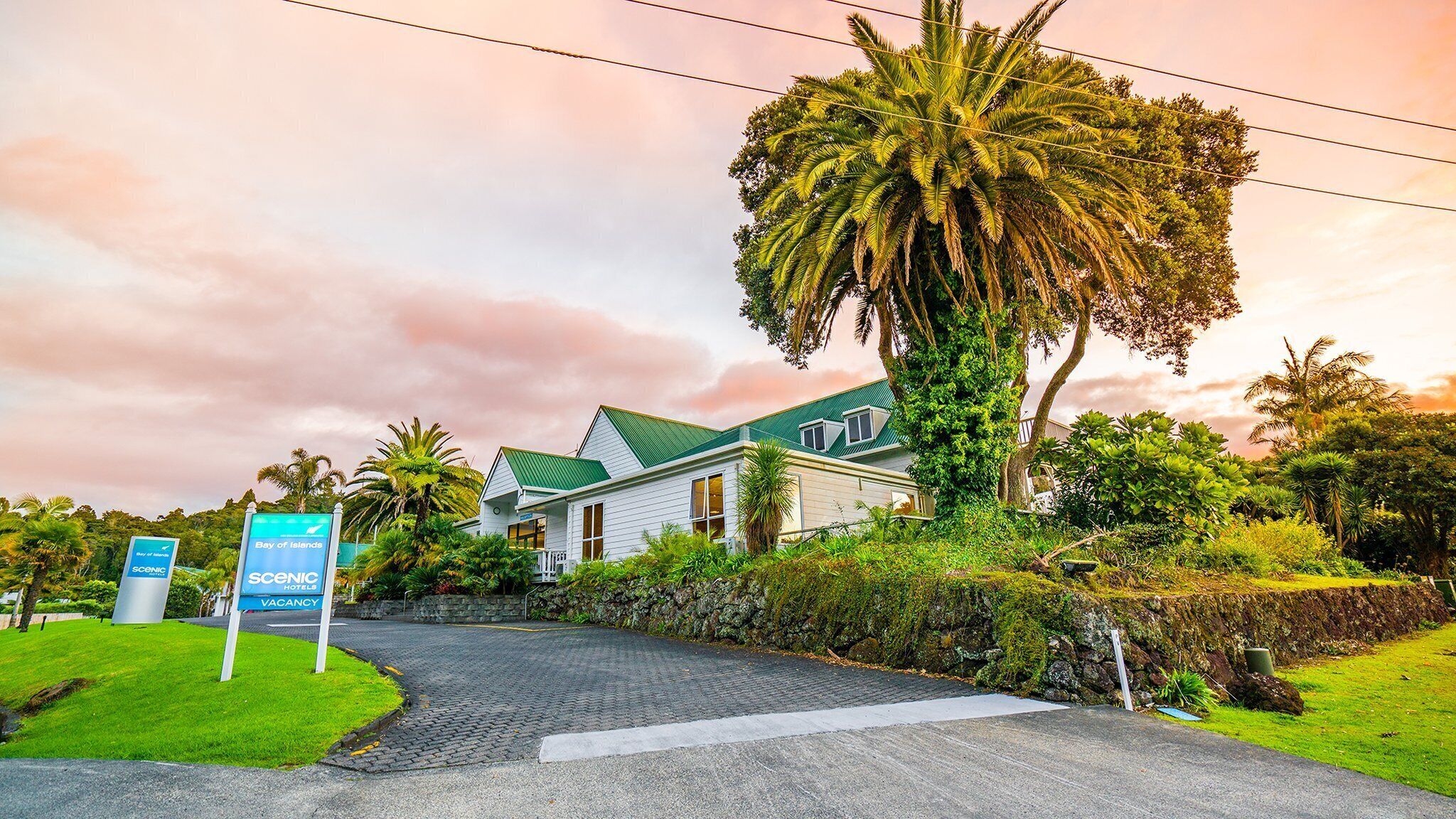 Un hotel con techo verde, rodeado de abundante vegetación y palmeras, con un cartel que indica que es un hotel panorámico.