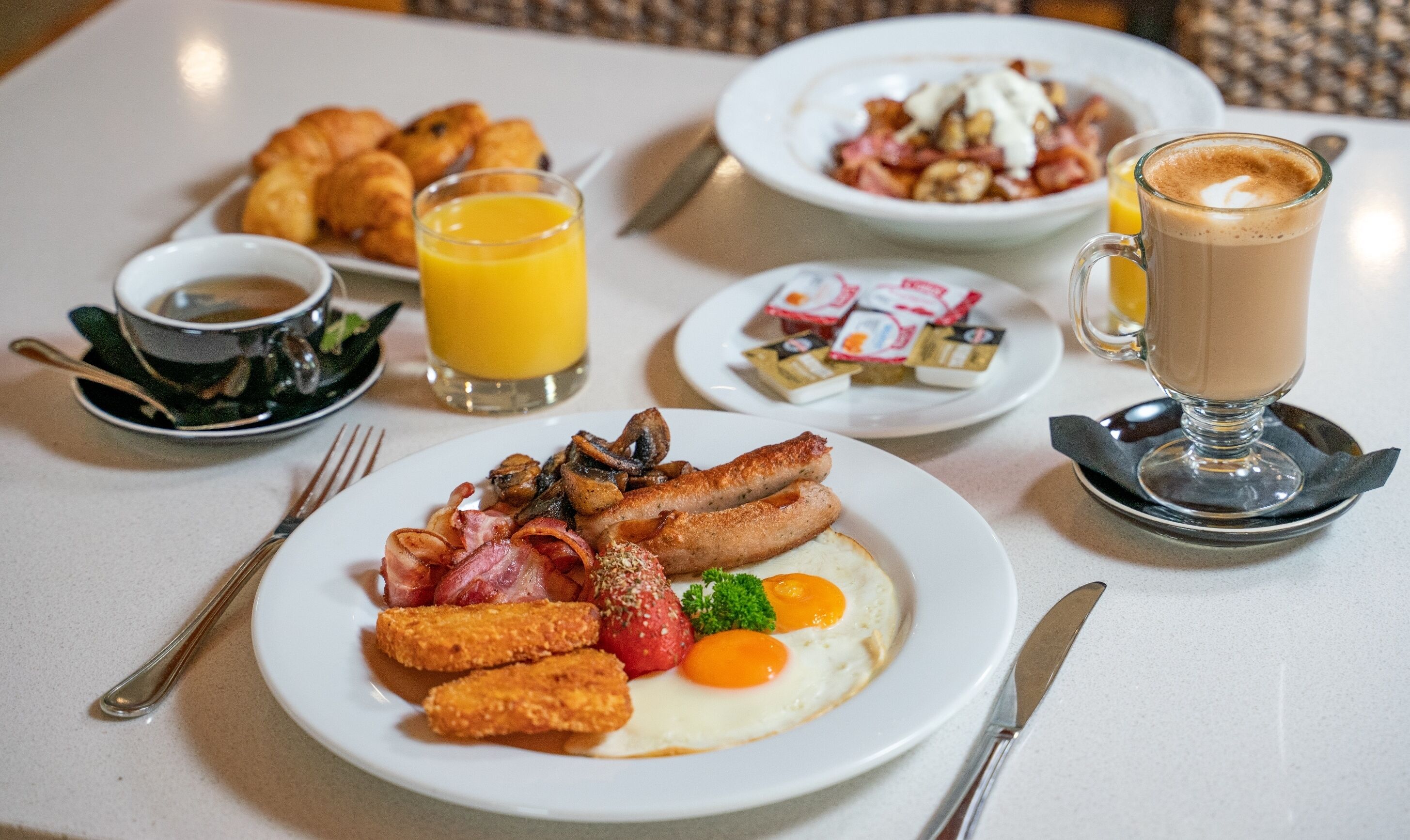 A breakfast table with plates of eggs, sausages, and toast, along with juice and coffee.