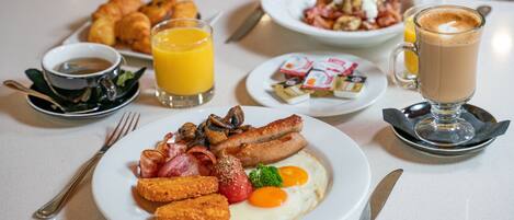 A breakfast table with plates of eggs, sausages, and toast, along with juice and coffee.