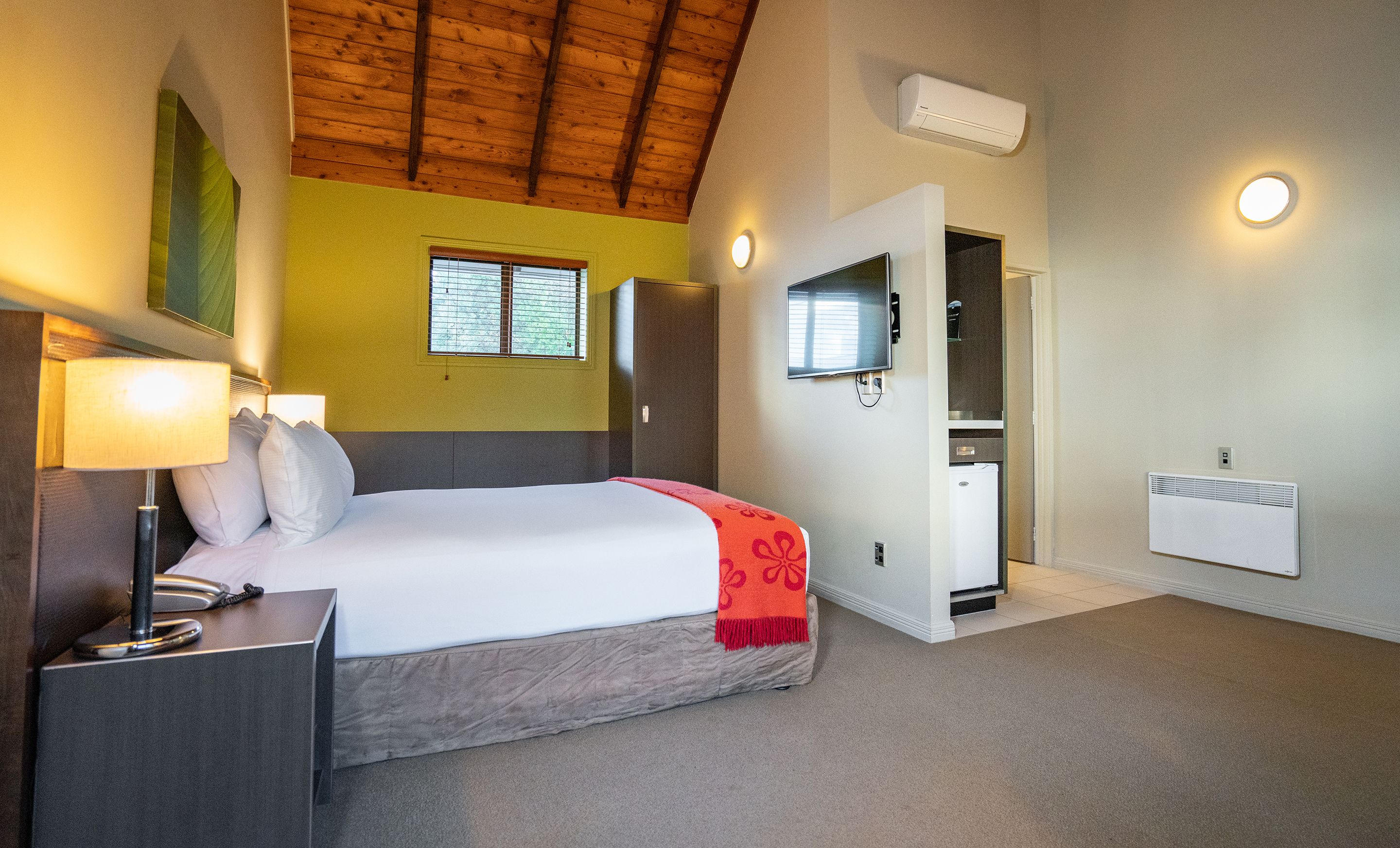 A bedroom with a bed, bedside table, lamp, and a window with blinds.