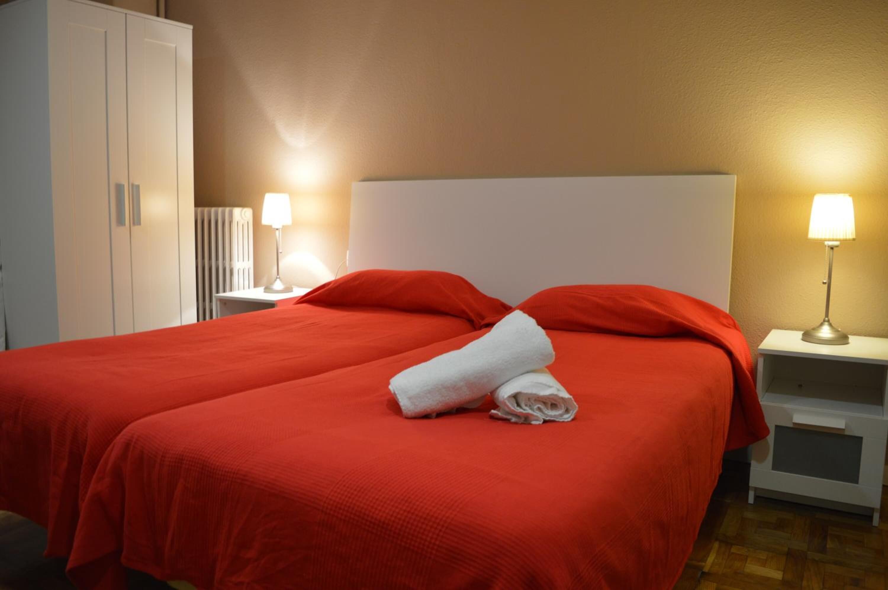 Een hotelkamer met een groot bed, twee nachtkastjes met lampen, een kledingkast en een radiator.