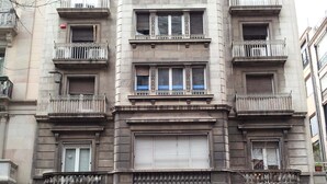A multi-story building with balconies, a green door, and outdoor seating with umbrellas. - Somnio Hostels (Barcelona)