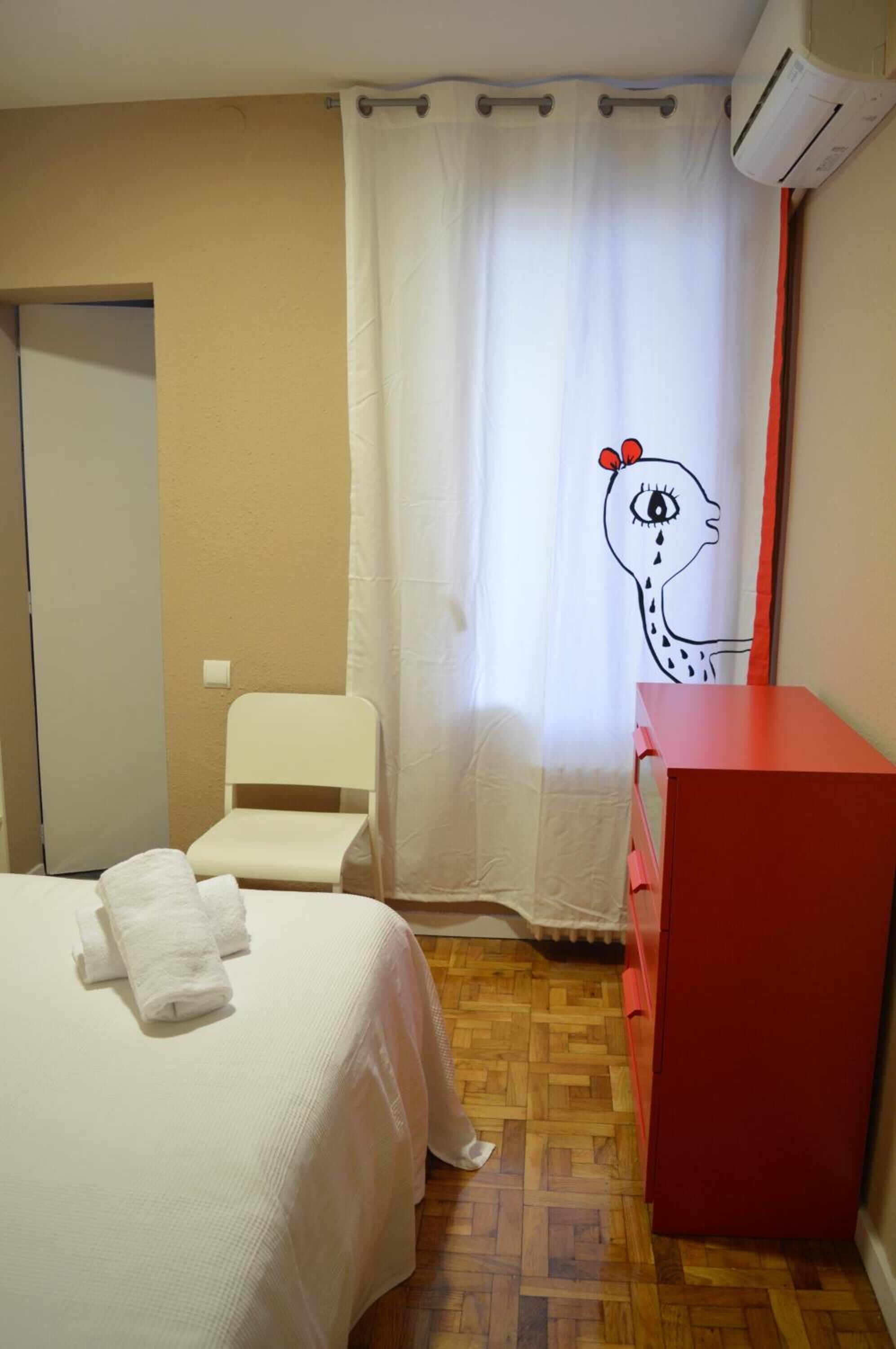 Un dormitorio con cama, una silla, un aparador rojo y una cortina con diseño de jirafa.