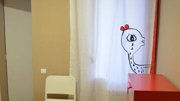 Un dormitorio con cama, una silla, un aparador rojo y una cortina con diseño de jirafa.