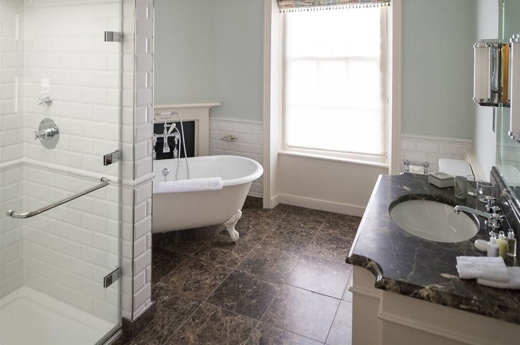 Une salle de bain dotée d’une baignoire sur pieds, d’un espace douche, d’un meuble-lavabo et d’une fenêtre laissant entrer la lumière naturelle.