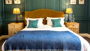 Un lit bien fait, recouvert d’une couverture bleue, avec deux oreillers et une tête de lit en bois. On y trouve deux tables de chevet avec des lampes, et un mur orné d’illustrations d’insectes encadrées.