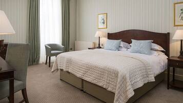 A hotel room with a large bed, two bedside tables with lamps, a chair, and a window with curtains.
