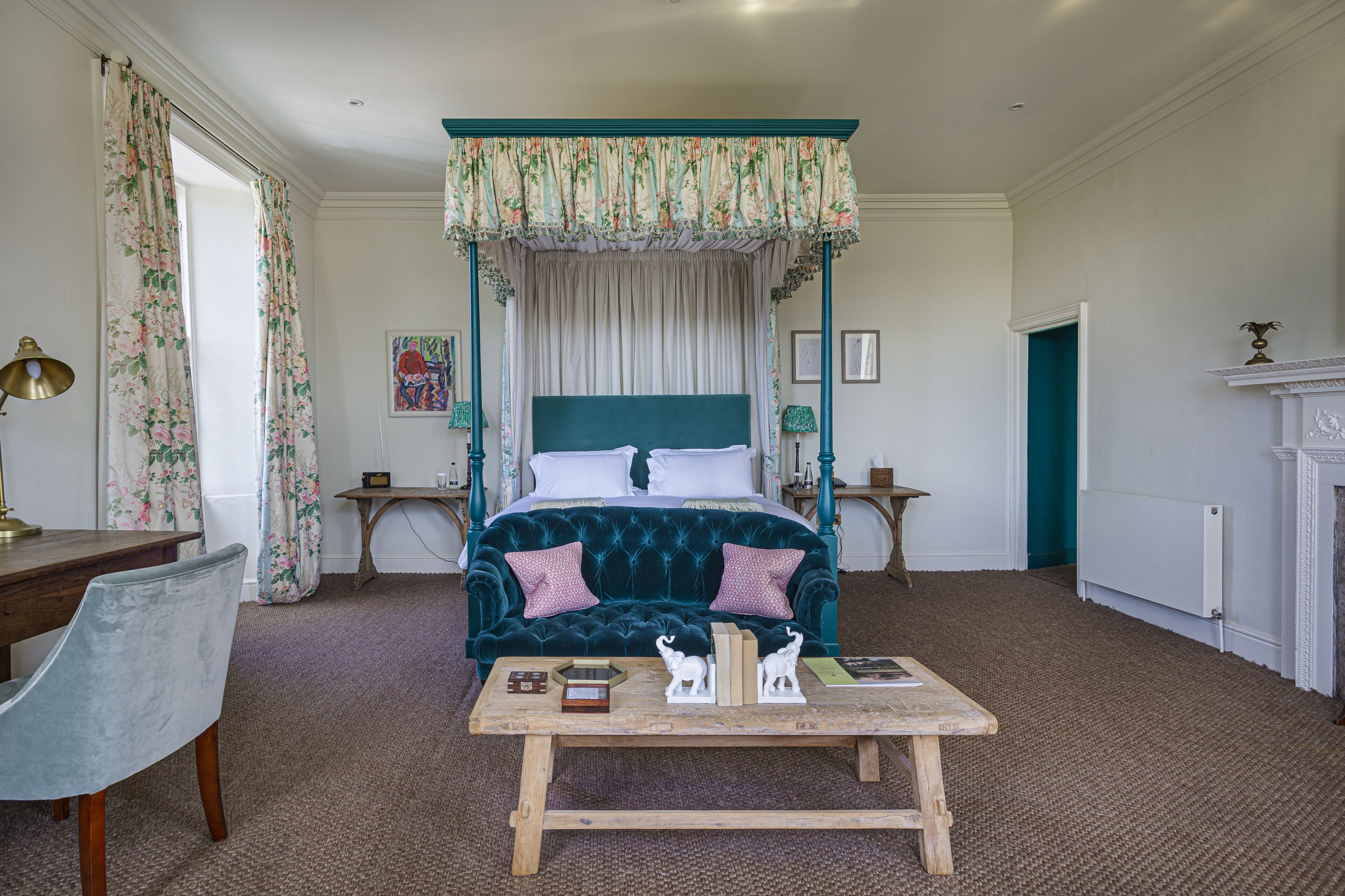 A bedroom with a four-poster bed, a wooden table with decorative items, a chair, and a fireplace.