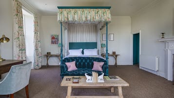 A bedroom with a four-poster bed, a wooden table with decorative items, a chair, and a fireplace.