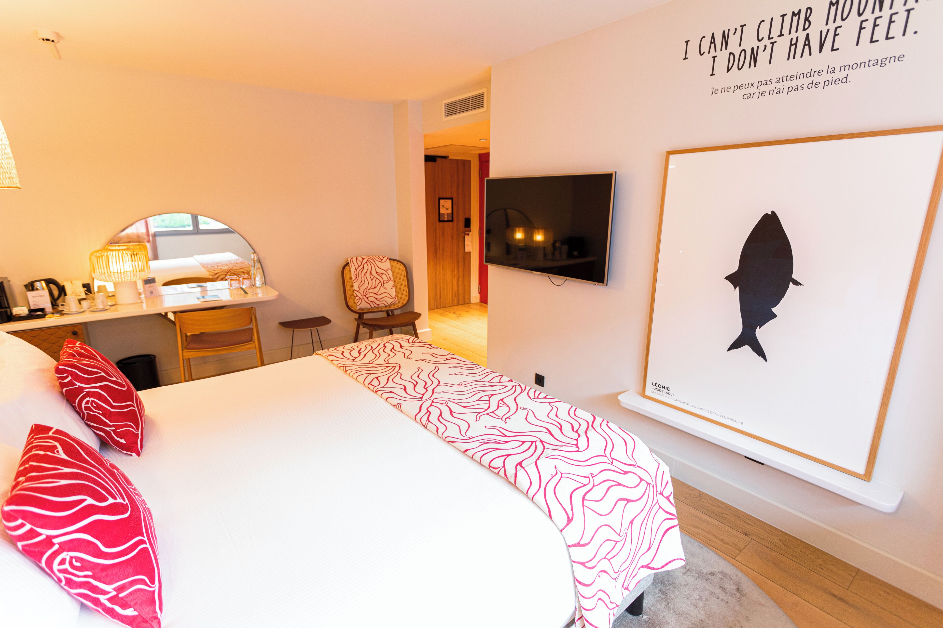 Habitación de hotel con una cama, un escritorio, una silla, un televisor y una silueta de pez en un marco en la pared.