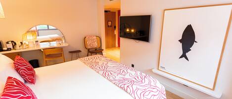 Habitación de hotel con una cama, un escritorio, una silla, un televisor y una silueta de pez en un marco en la pared.