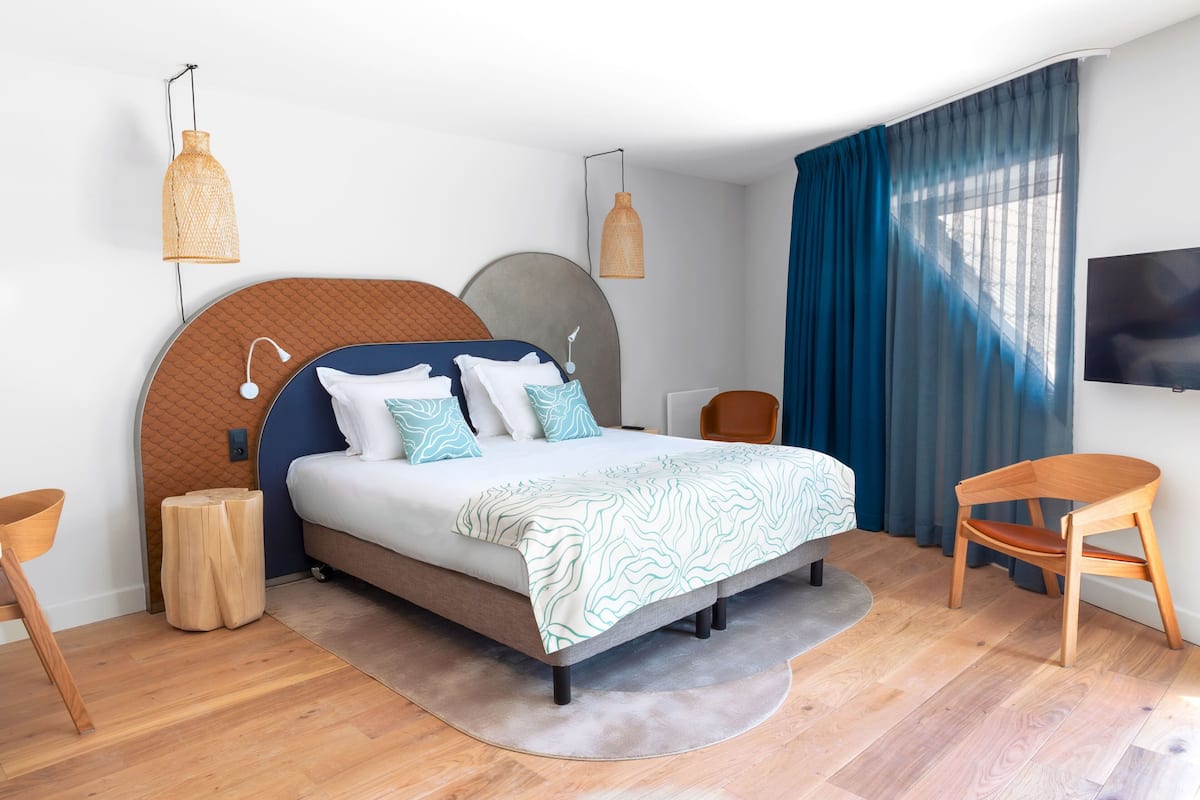 Une chambre à coucher moderne, avec un lit, deux tables de chevet, une chaise, un téléviseur et une grande fenêtre avec des rideaux.