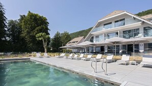 Un hotel moderno con piscina, tumbonas y vistas al bosque circundante.