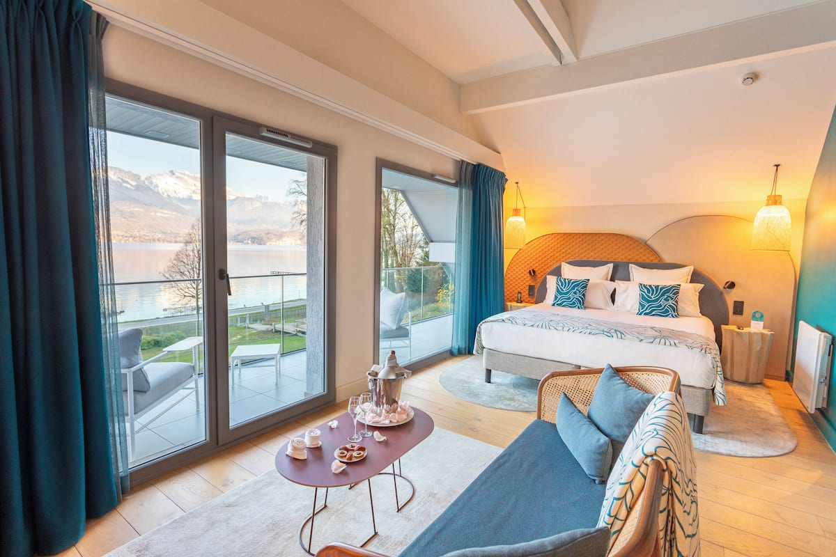 Une chambre avec un lit, un canapé, une table sur laquelle se trouve un plateau de nourriture, et une vue sur un lac et des montagnes.