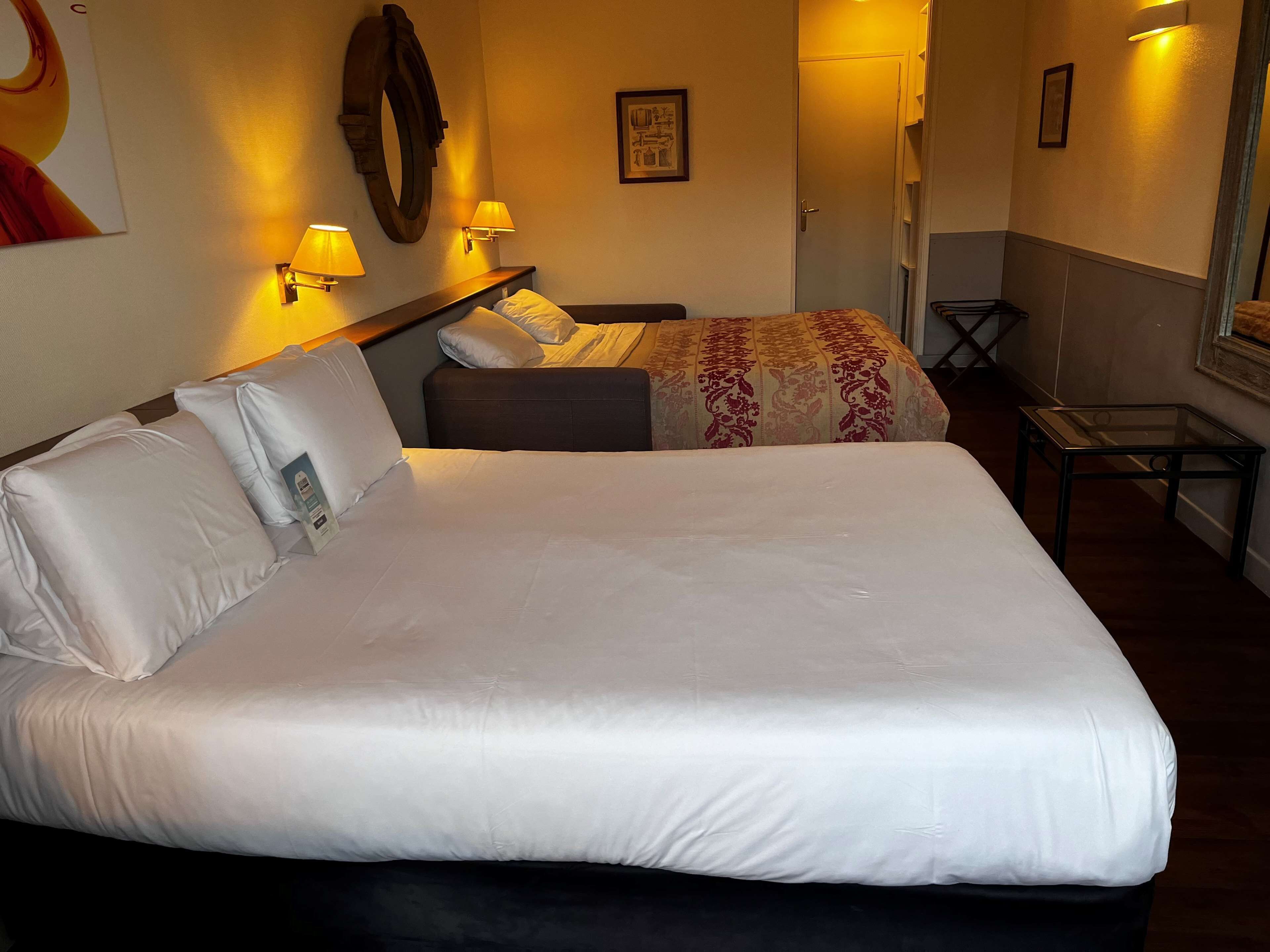 Quarto de hotel com uma cama grande, duas mesas de cabeceira com abajures, uma pequena escrivaninha e uma cadeira.