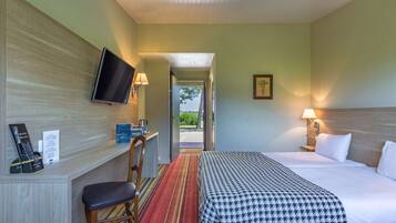 A hotel room with a bed, a desk with a chair, a television, and a view of the outdoors.