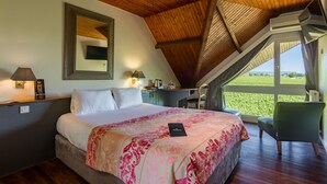 A bedroom with a large bed, a desk, and a chair. There is a window with a view of a green field. - KYRIAD PRESTIGE BEAUNE - Le Panorama (Beaune)