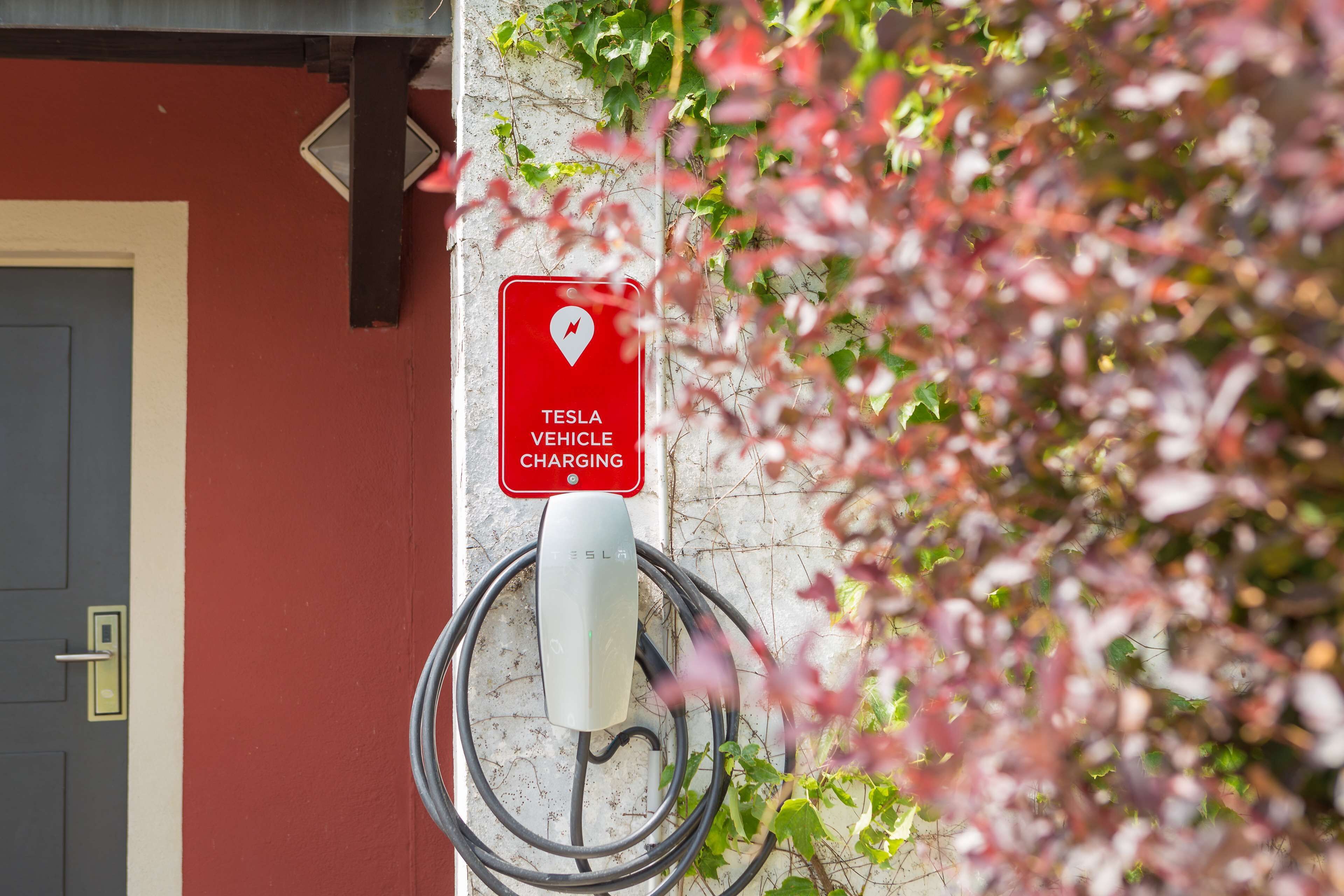 A Tesla vehicle charging station mounted on a wall with a red sign indicating charging availability.
