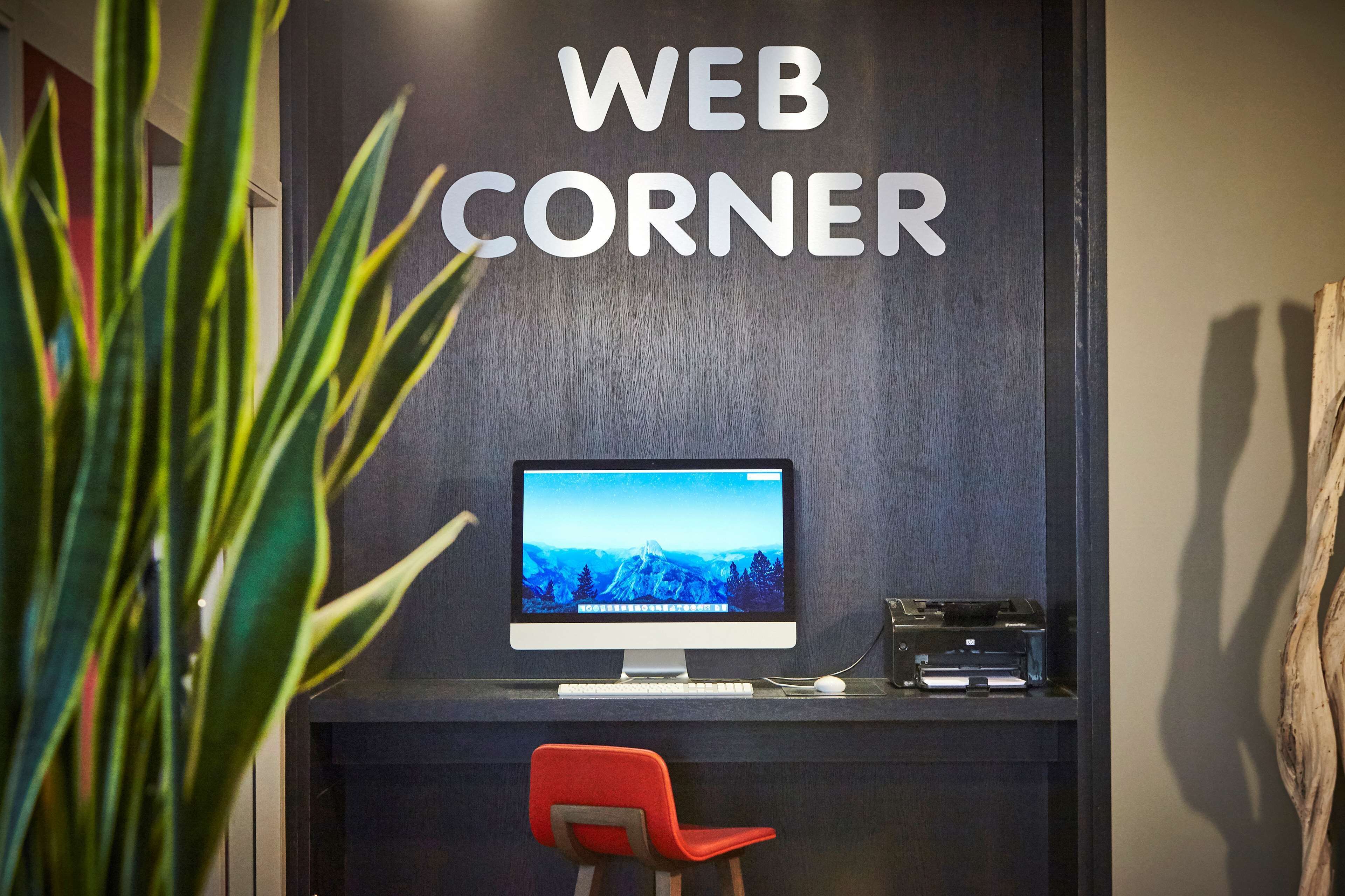 Escritorio con computadora, monitor, teclado e impresora, una silla roja y un letrero en la pared que dice 