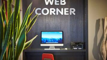 Escritorio con computadora, monitor, teclado e impresora, una silla roja y un letrero en la pared que dice