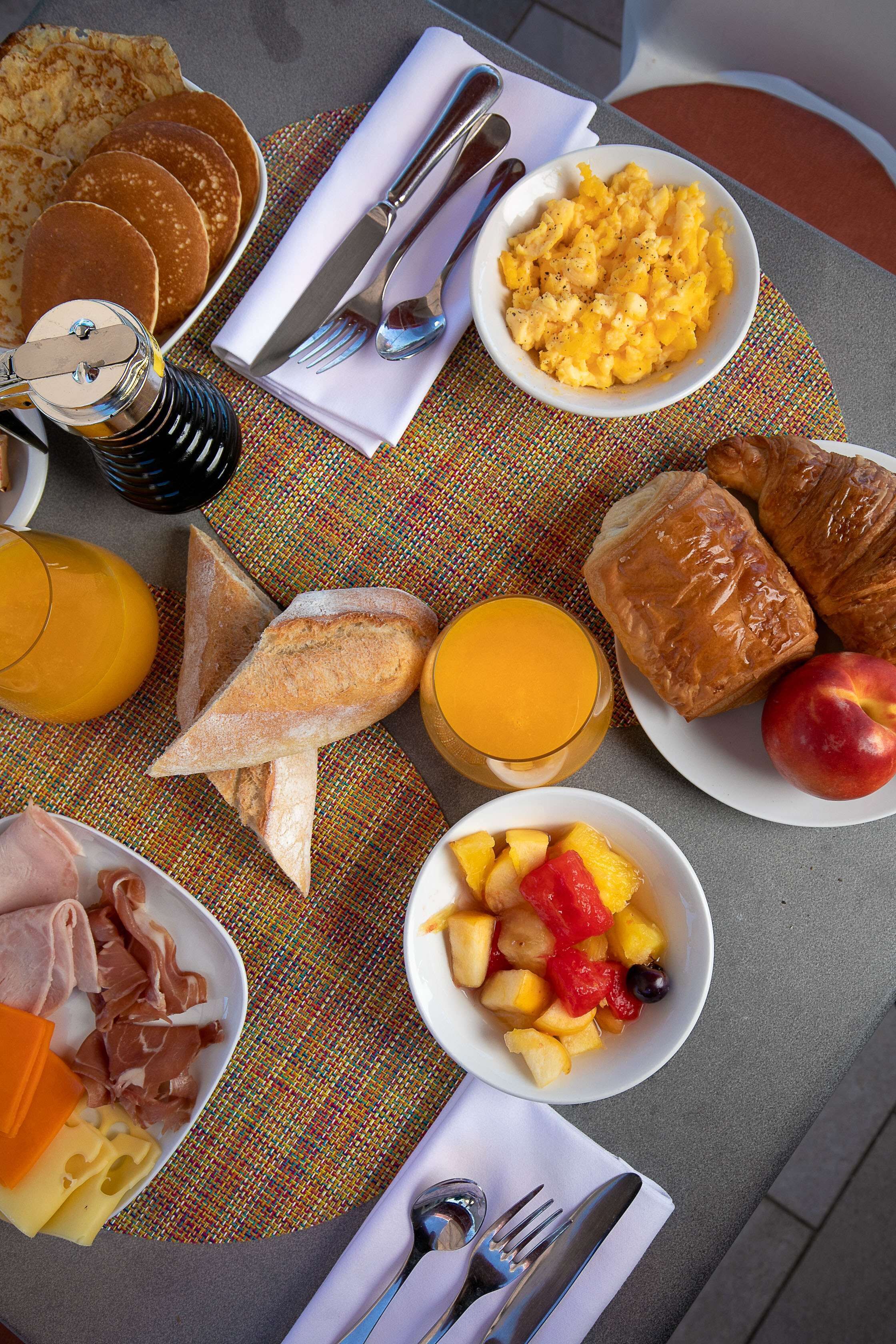 Ein Frühstückstisch mit Pfannkuchen, Rührei, Croissants, Obst und Käse.