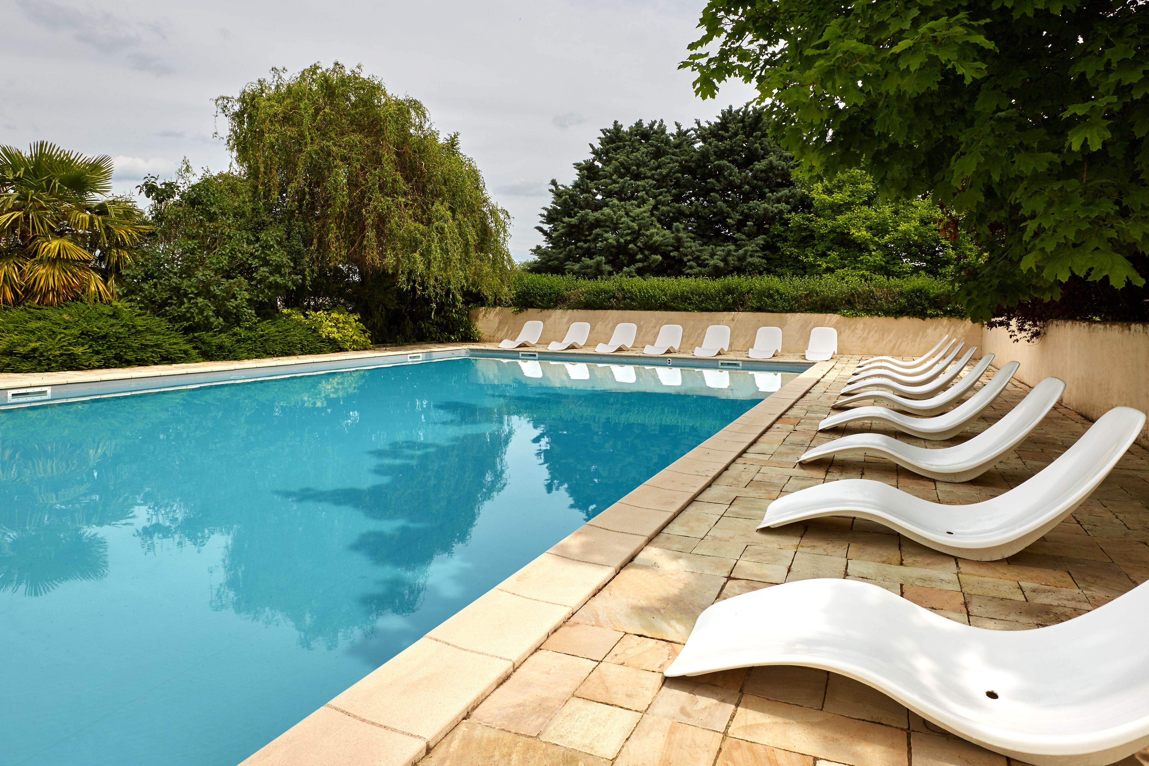 Una piscina con sillones de descanso blancos a lo largo de la orilla.