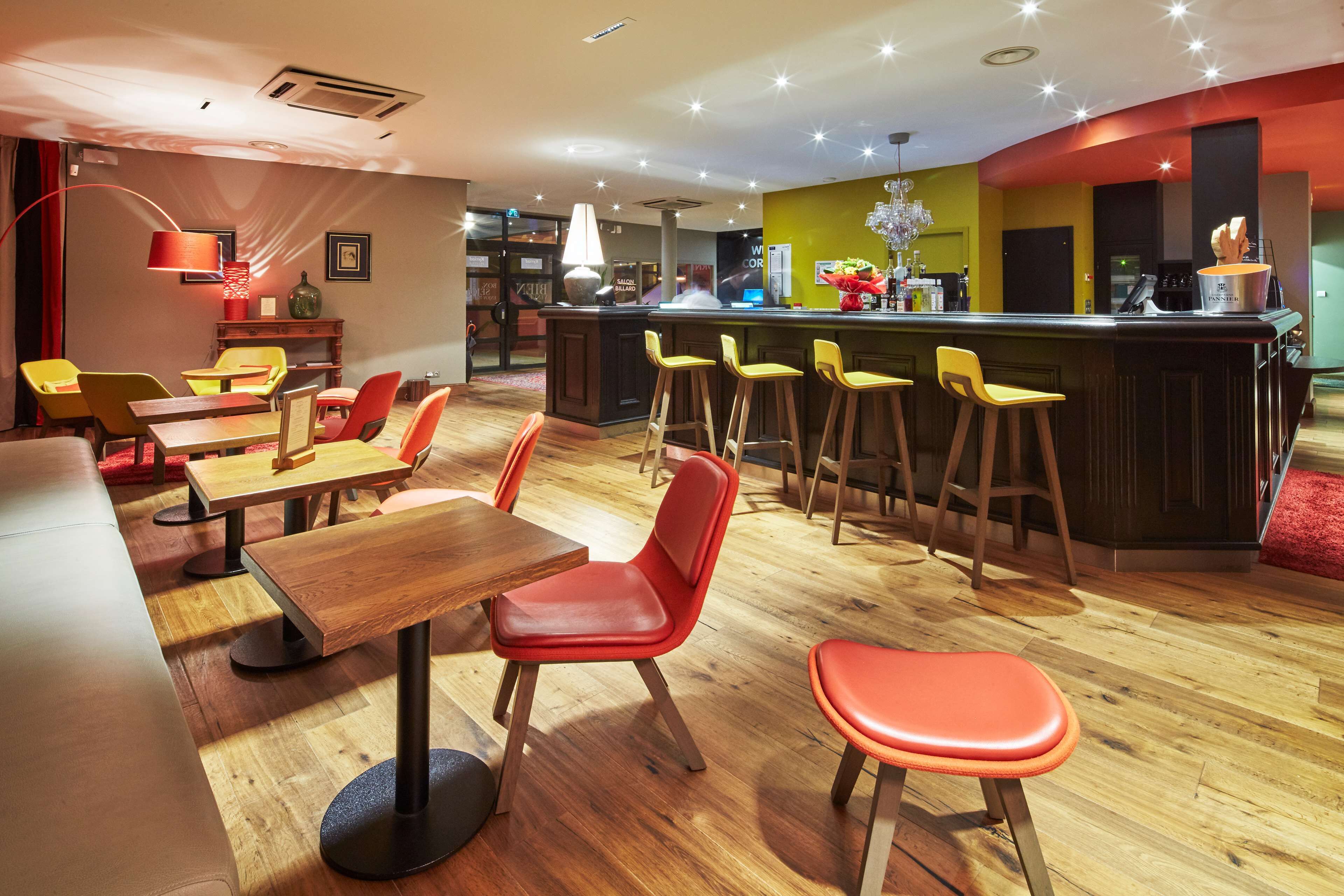 Ein Restaurant mit Holztischen und roten Stühlen, ein Barbereich mit Hockern und eine Theke mit einer Registrierkasse.