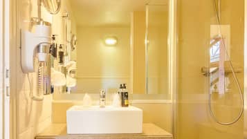 Un baño con lavamanos, espejo, toallero y ducha.