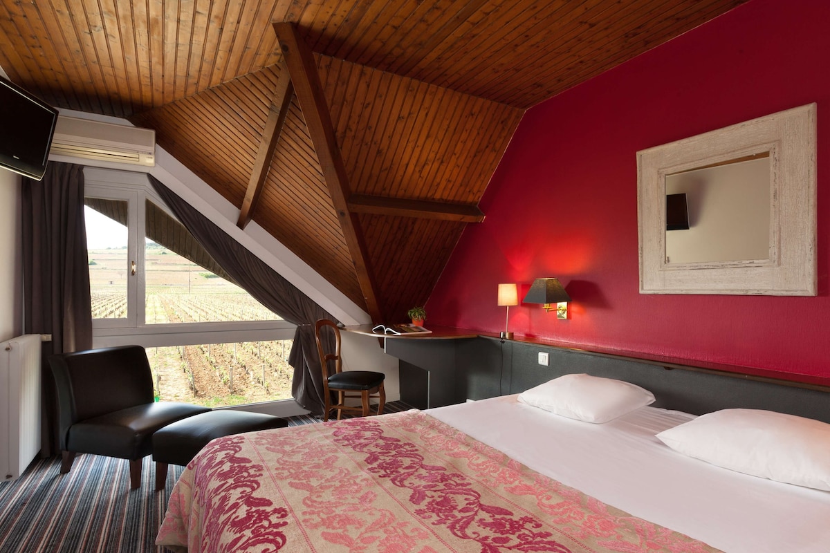Habitación de hotel con una cama grande, un escritorio, una silla y una ventana con vistas al campo.