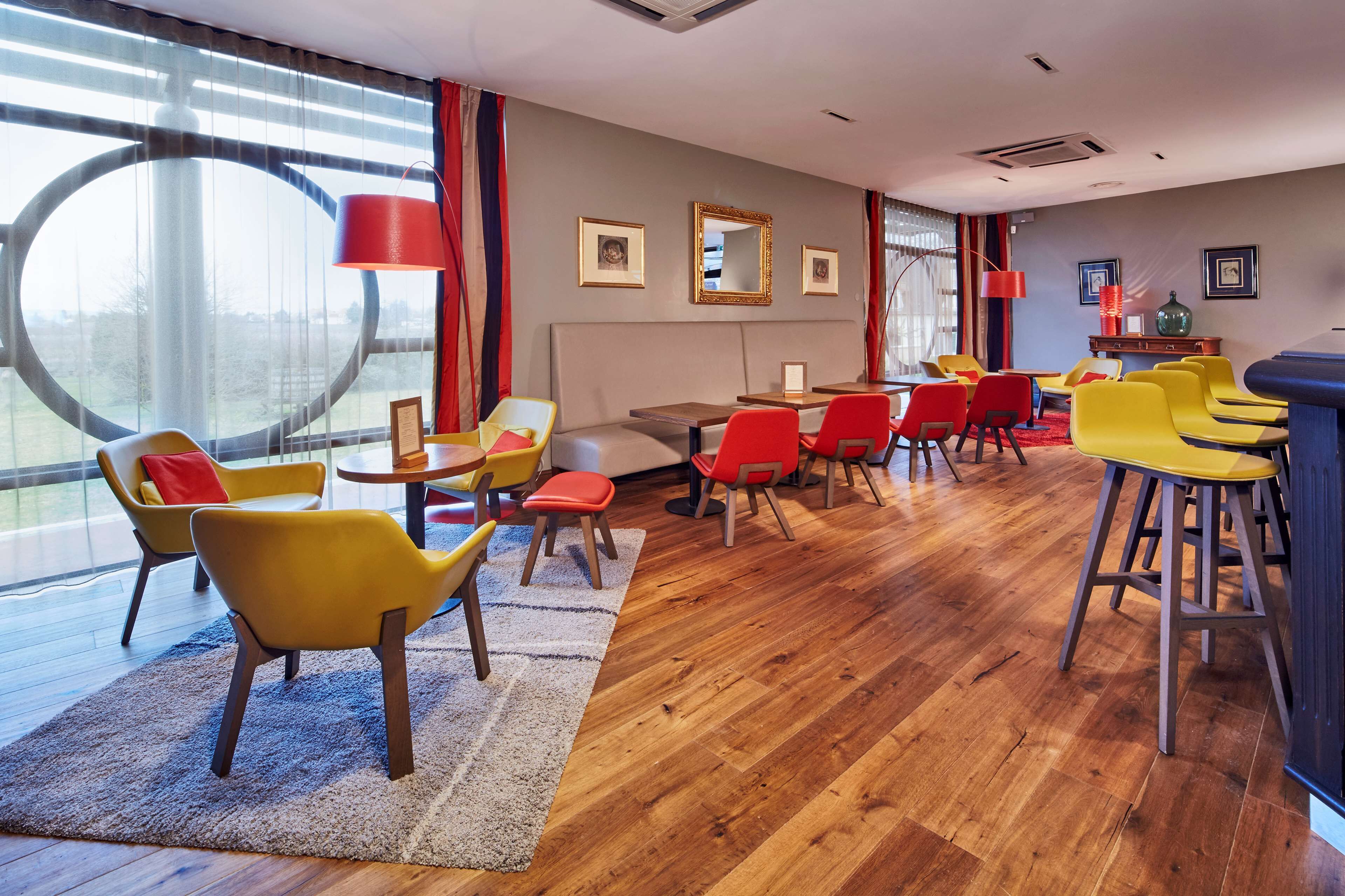 Une chambre d’hôtel moderne avec une grande fenêtre, un plancher en bois et un mélange de chaises jaunes et rouges.