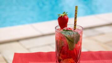 Un vaso de bebida helada con fresa y adornos de menta sobre un tapete rojo junto a una piscina.