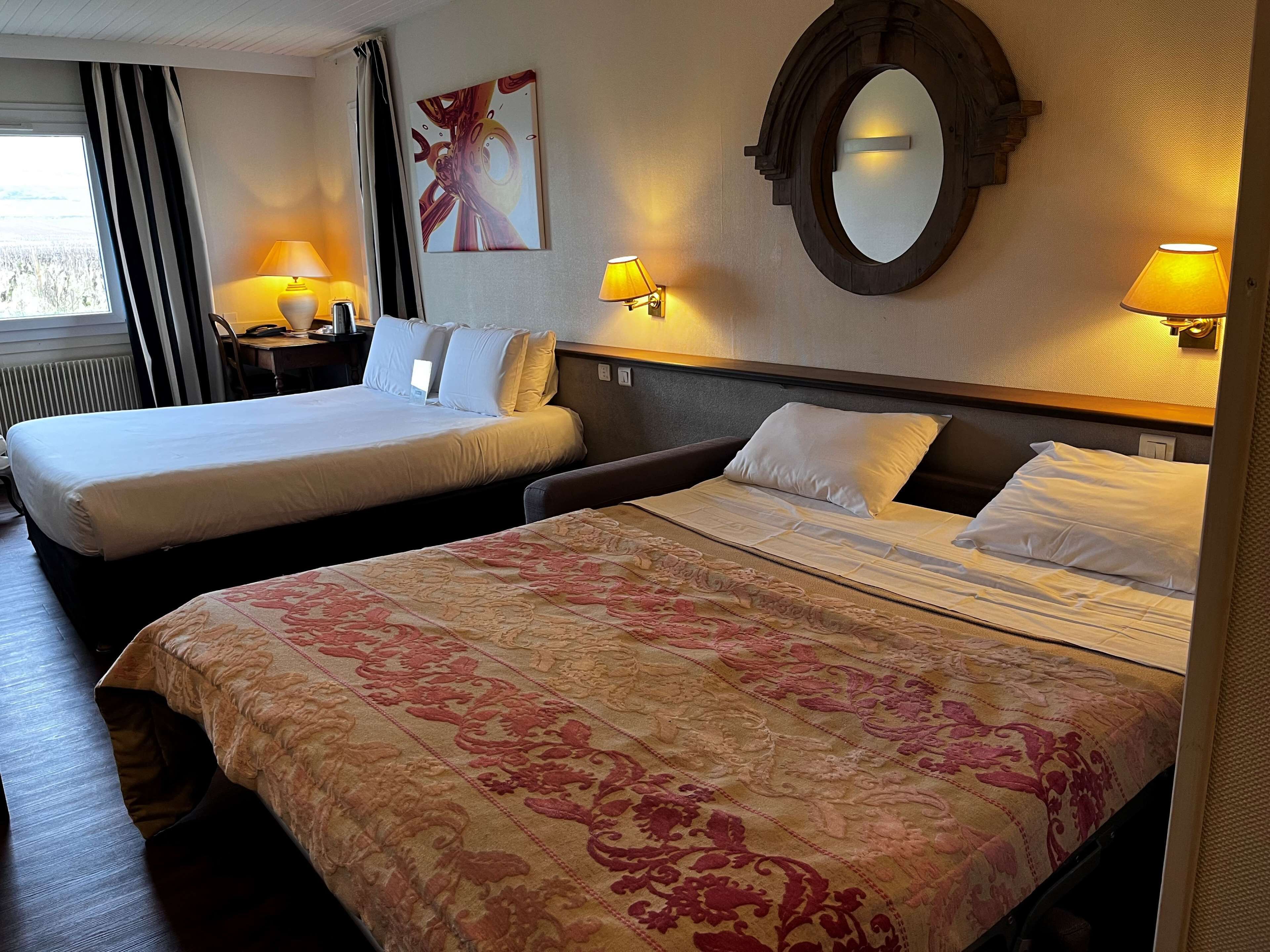 Een hotelkamer met twee bedden, een grote spiegel en twee wandlampen.
