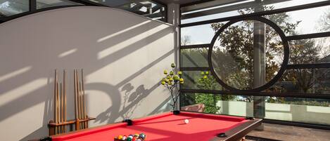 A pool table with balls, a cue stick rack, and a decorative vase with yellow flowers.