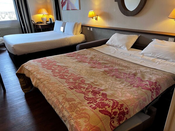 A hotel room with two beds, a large floral bedspread, bedside lamps, and a round mirror on the wall. - KYRIAD PRESTIGE BEAUNE - Le Panorama (Beaune)