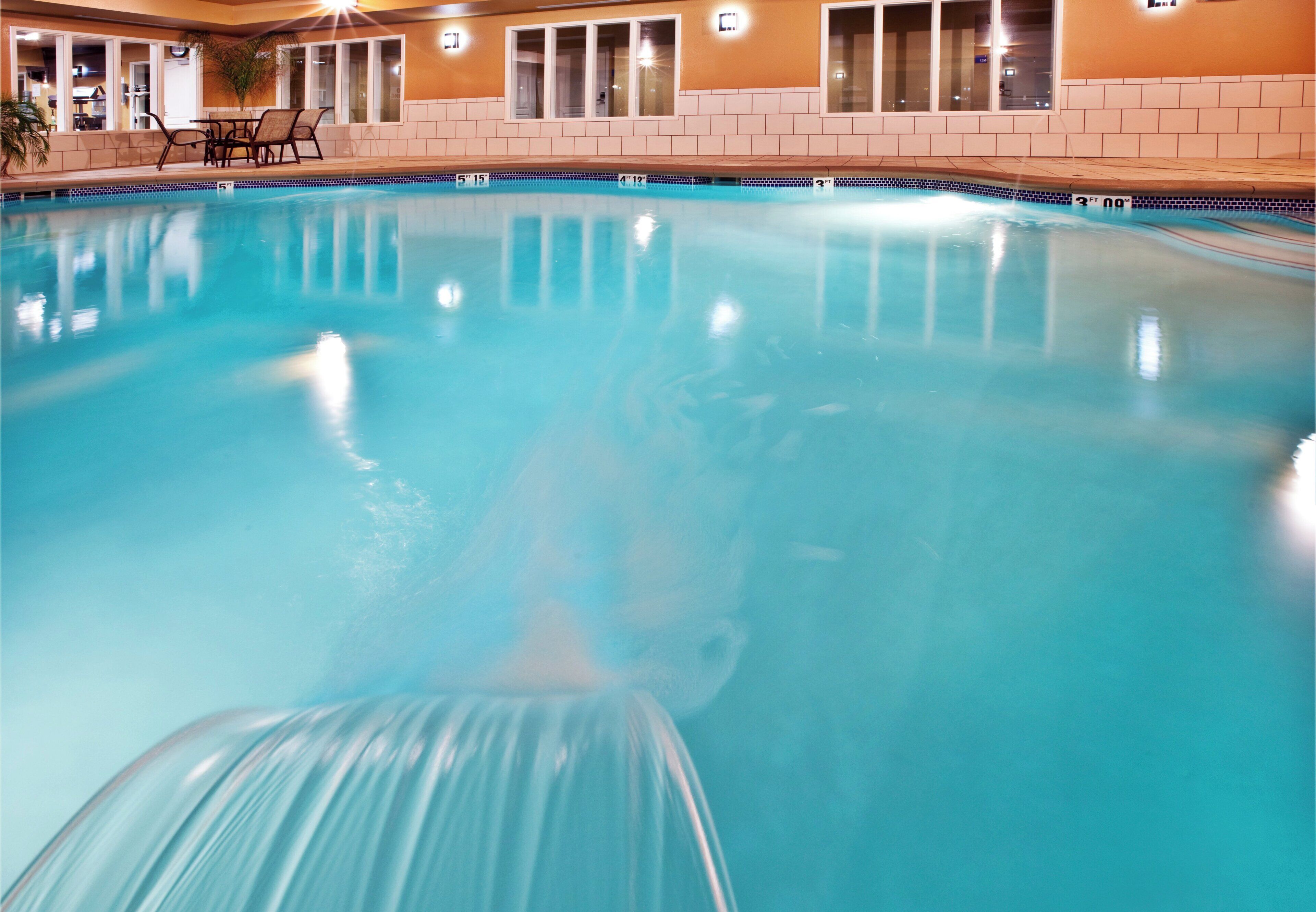 A swimming pool with clear water, surrounded by a tiled wall and a window.