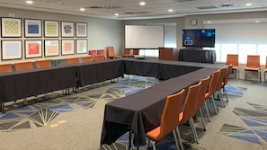 A conference room with a long table, orange chairs, a projector screen, and framed artwork on the wall. - Holiday Inn Express Hotel & Suites Crawfordsville by IHG (Crawfordsville)