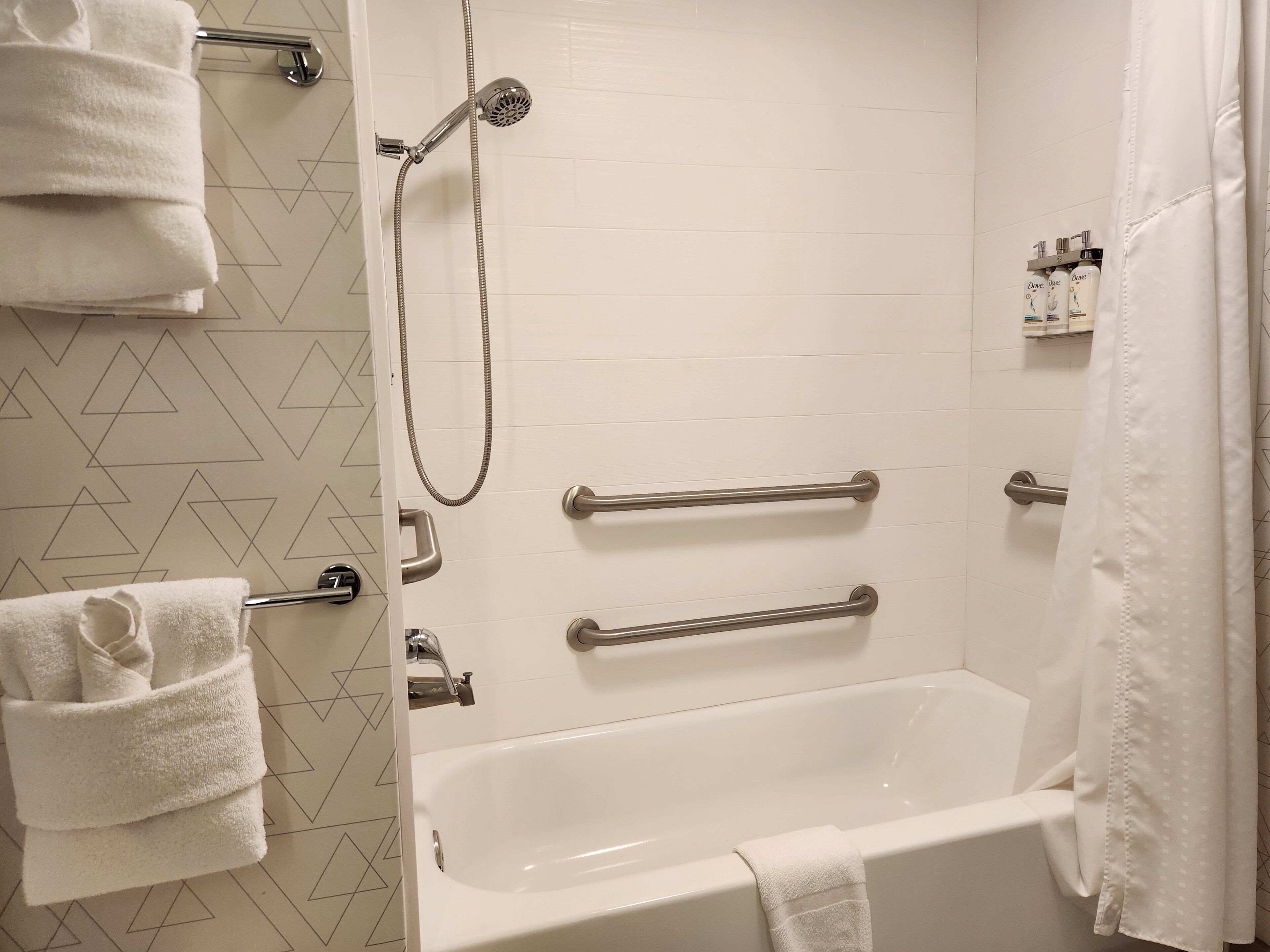 A bathroom with a bathtub, a shower, and handrails. There are towels and toiletries on the wall.