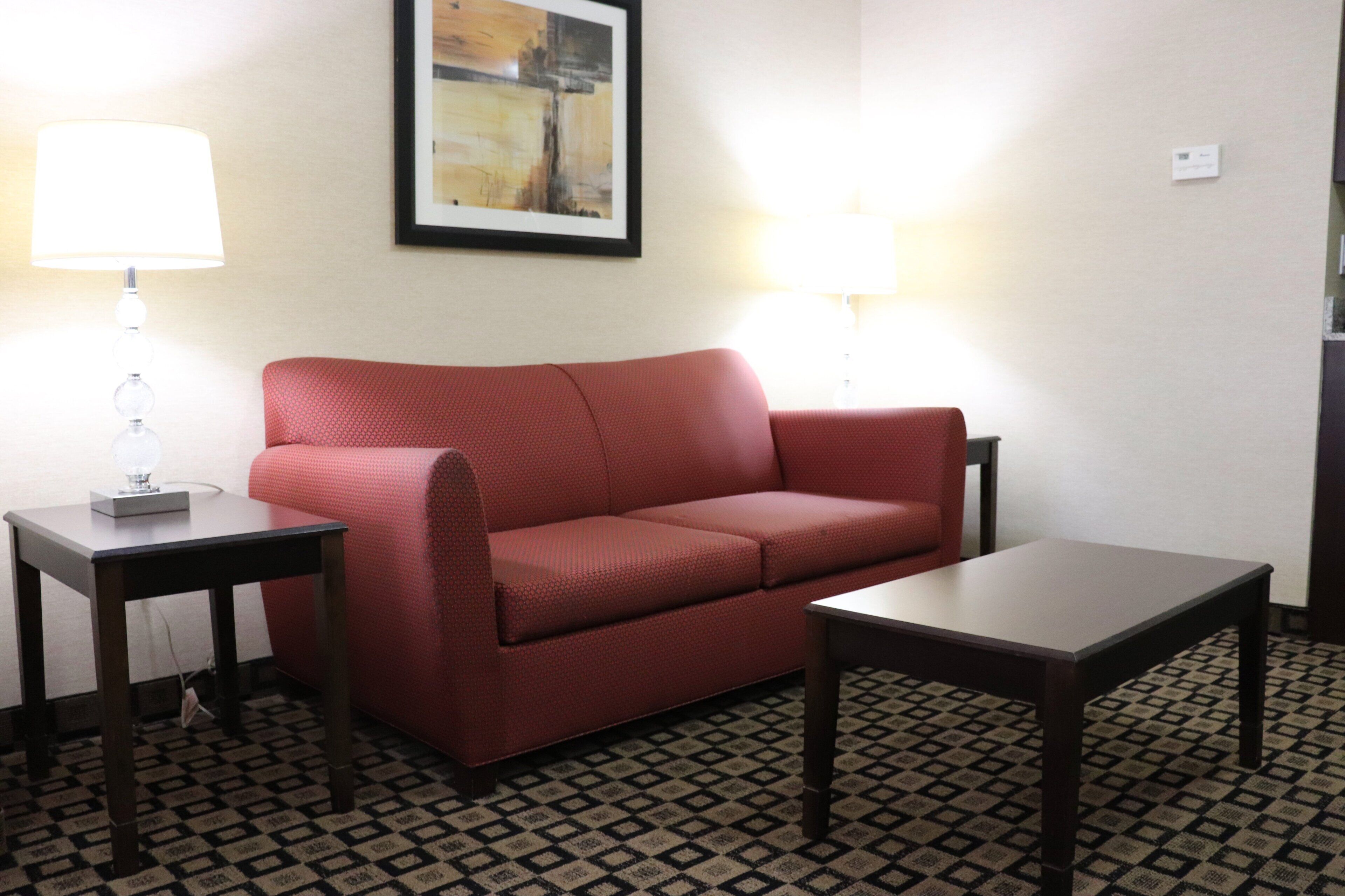 A room with a red sofa, two side tables with lamps, a framed artwork on the wall, and a patterned floor.