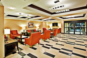 A hotel lobby with a checkered floor, seating area with tables and chairs, and a television mounted on the wall. - Holiday Inn Express Hotel & Suites Crawfordsville by IHG (Crawfordsville)